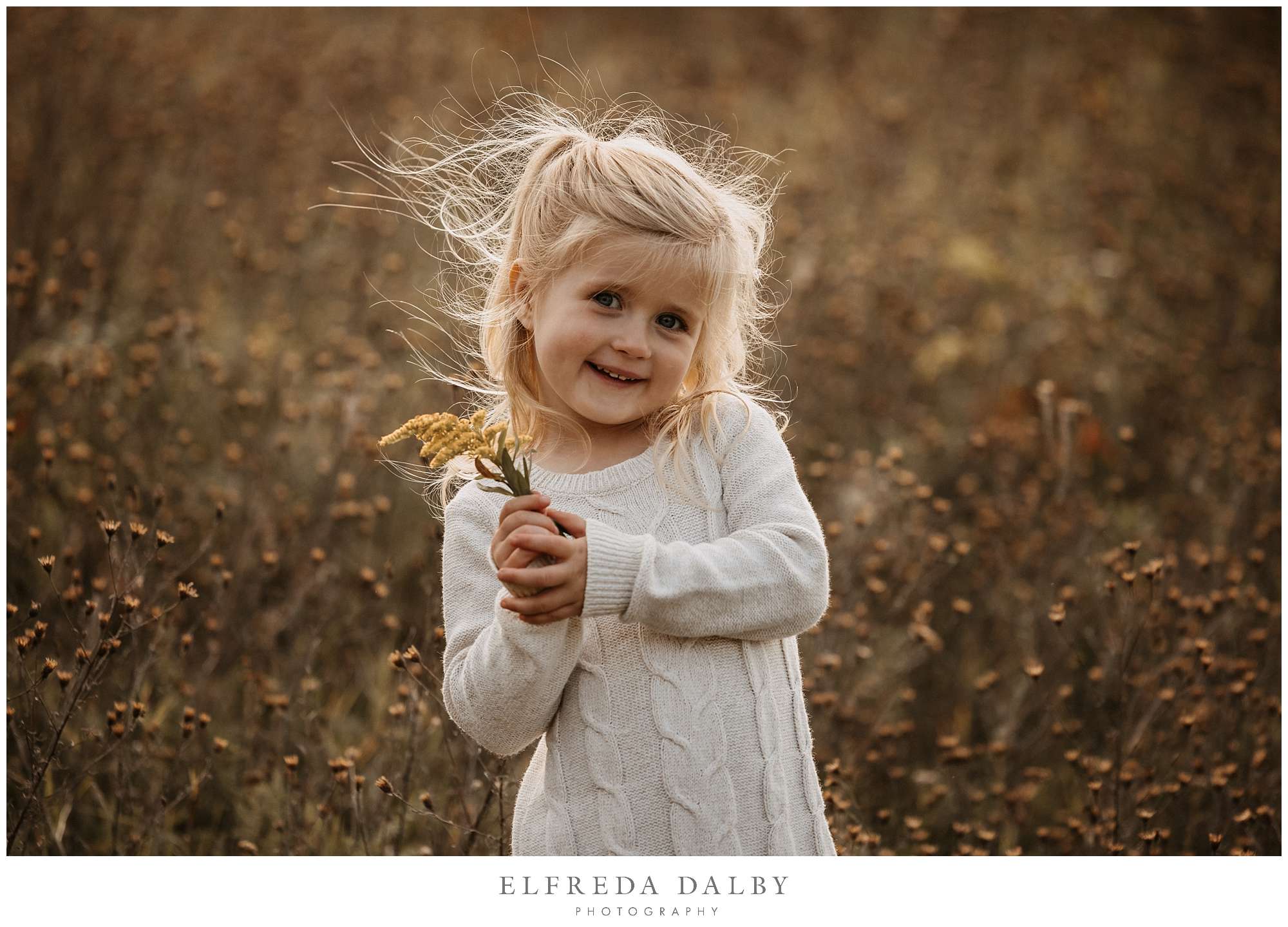 A cute little girl holding a flower in a field during golden hour